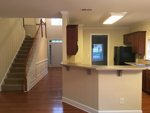 A kitchen with a black fridge and microwave, a wooden counter and a staircase with a brown railing.